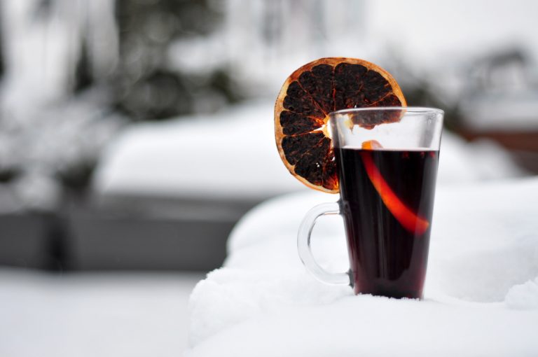 Warm glass of red mulled wine dried oranges resting in the thick snow, by Art In Voyage